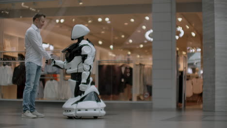 Ein-Mann-Steht-Mit-Einem-Roboterbot-Zusammen-Und-Stellt-Ihm-Fragen-Und-Bittet-Um-Hilfe,-Indem-Er-Auf-Dem-Bildschirm-Auf-Den-Roboterkörper-Klickt.-Mensch-Roboter-Interaktion-In-Der-Modernen-Welt